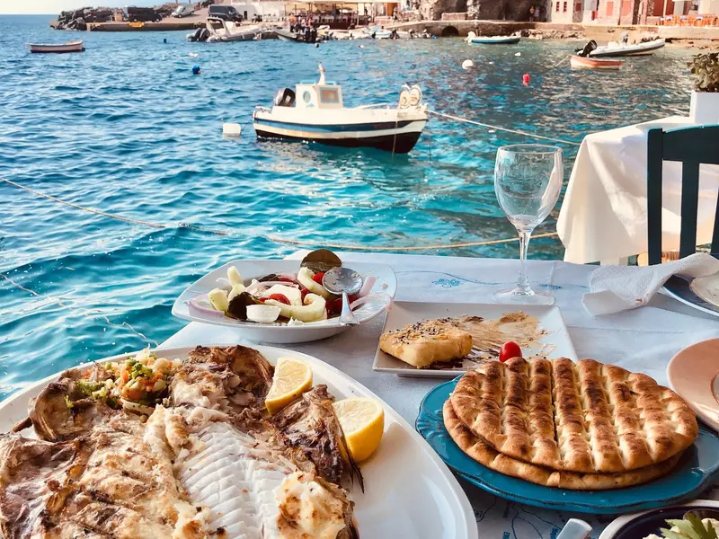Grilled fish, salad, bread and fries on a table by the sea.