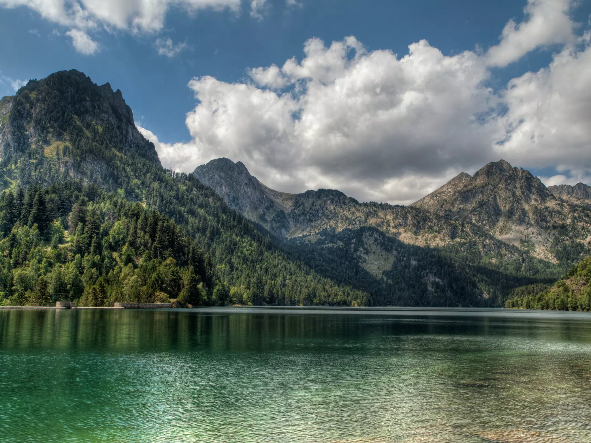 A tranquil lake surrounded by mountains with clouds and blue sky above.