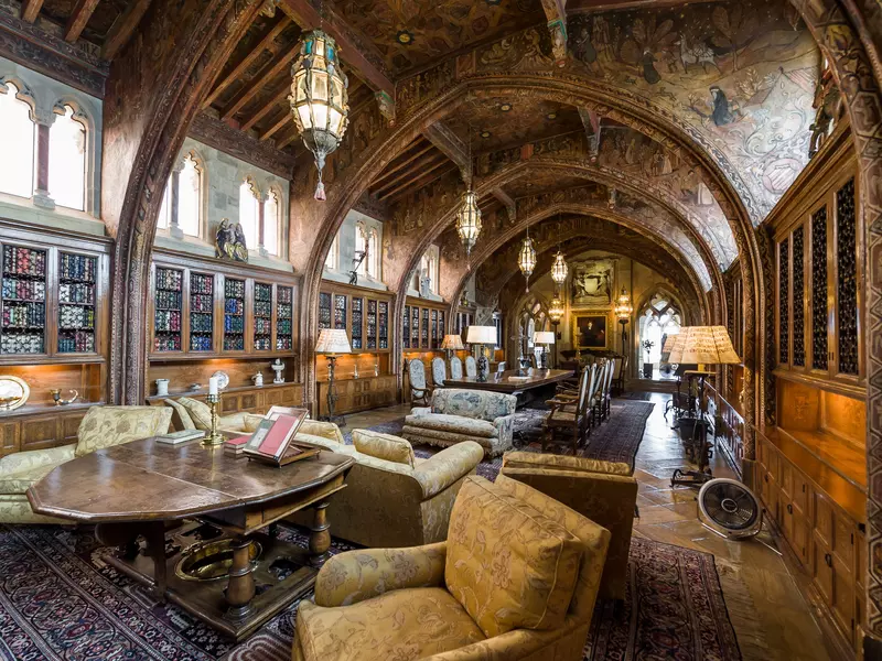 An elaborate library lined with books, filled with plush chairs and topped with a vaulted ceiling