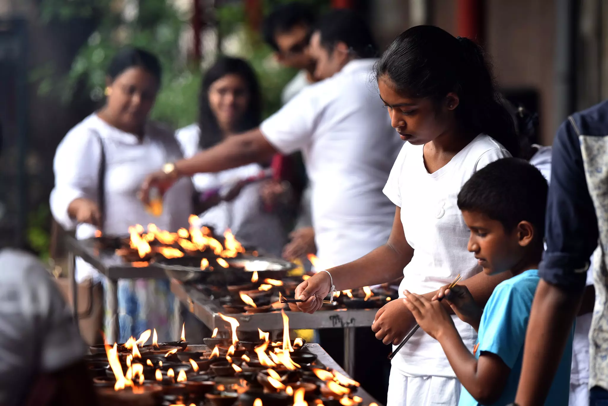 A boy and girl light sticks over fire with adults in the background