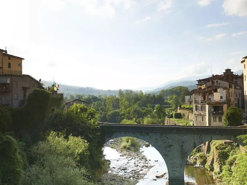 A rustic bridge crosses a river in the Tuscan countryside. 