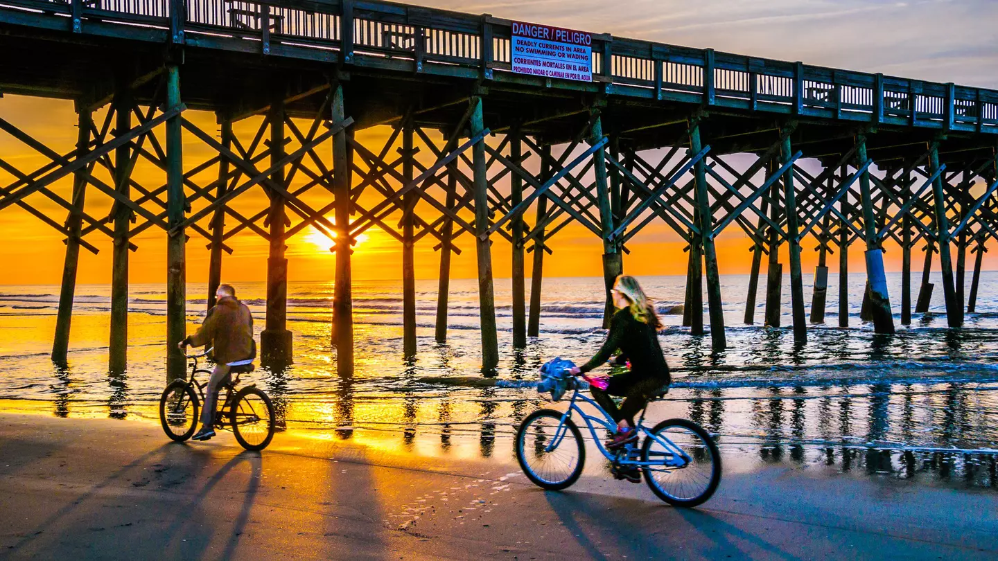 A mature couple ride their bicycles beneath Folly Beach Pier, South Carolina