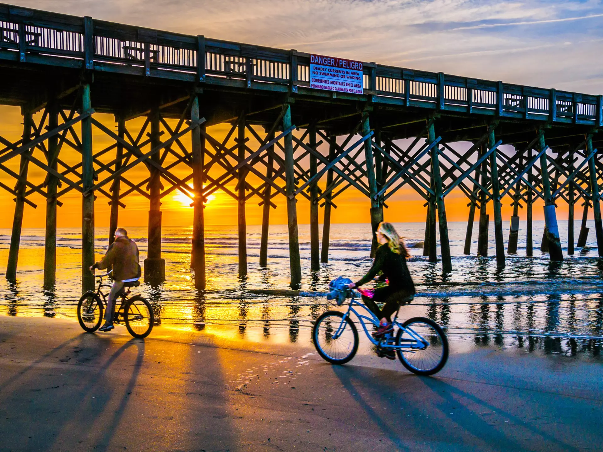 A mature couple ride their bicycles beneath Folly Beach Pier, South Carolina