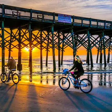 A mature couple ride their bicycles beneath Folly Beach Pier, South Carolina