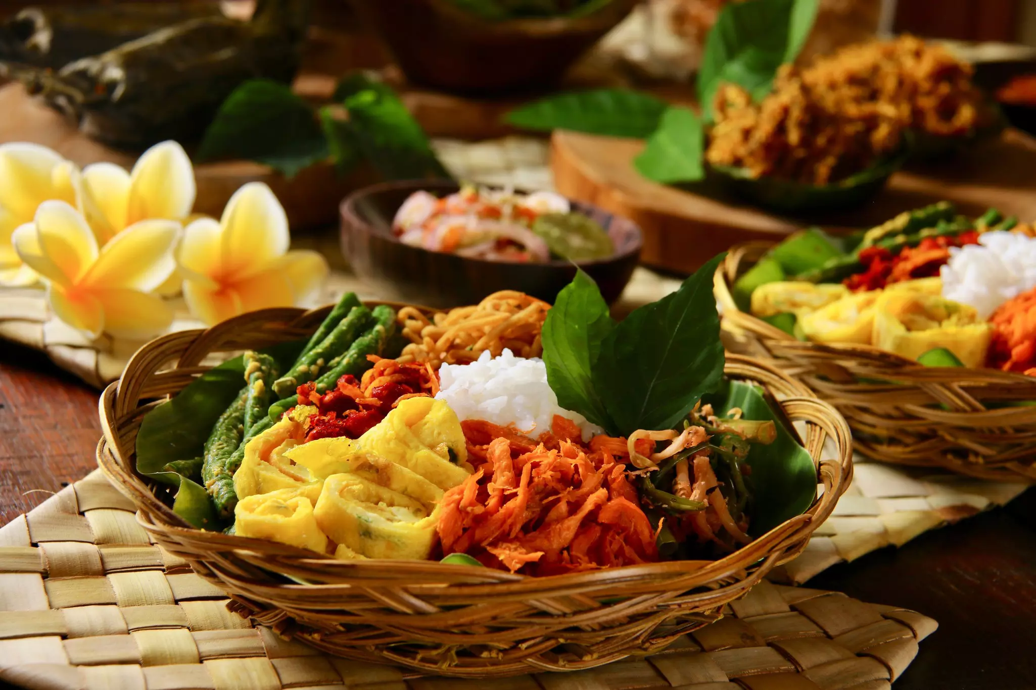 Nasi Campur Bali, a Balinese meal of rice with a variety of side dishes, shown in a wicker bowl near other food bowls