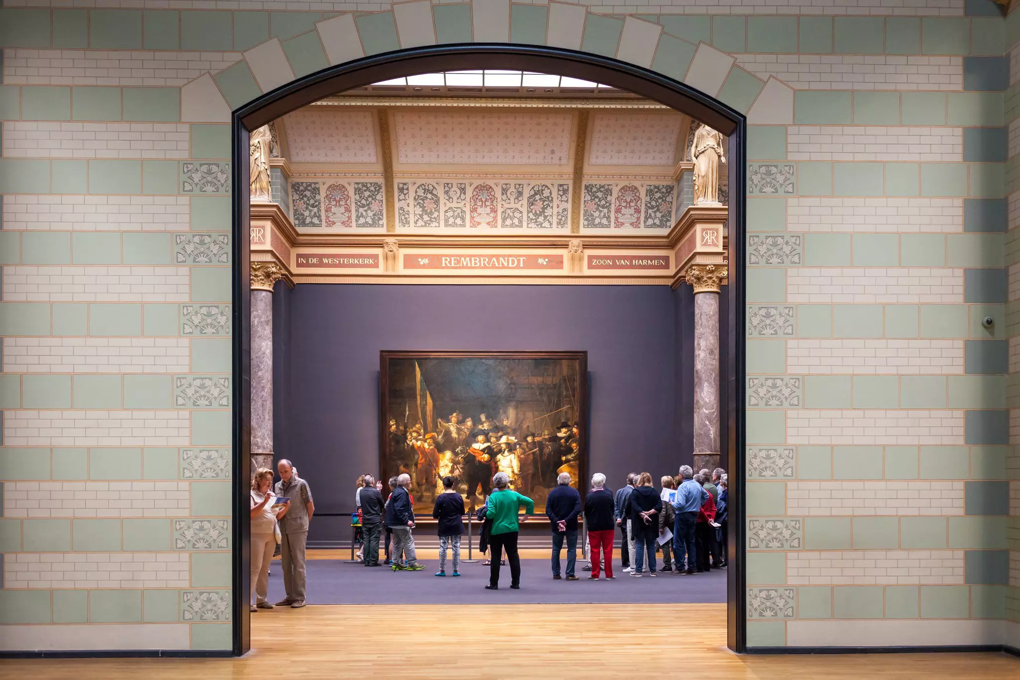 People are seen in a grand gallery looking at large-format painting.