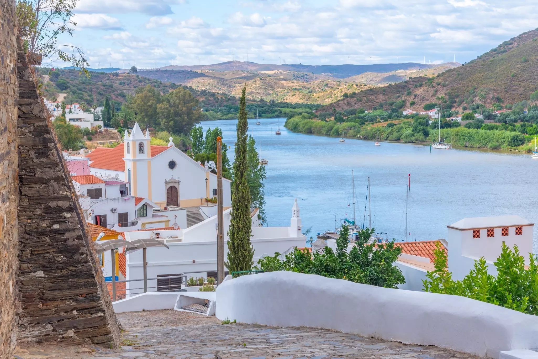 A path leading down to a town of white buildings along a river.