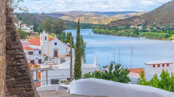 A path leading down to a town of white buildings along a river.