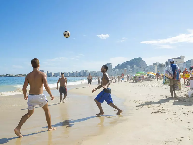 Young carioca Brazilians play a game of altinho beach football keepie uppie on the shore of Copacabana Beach. 