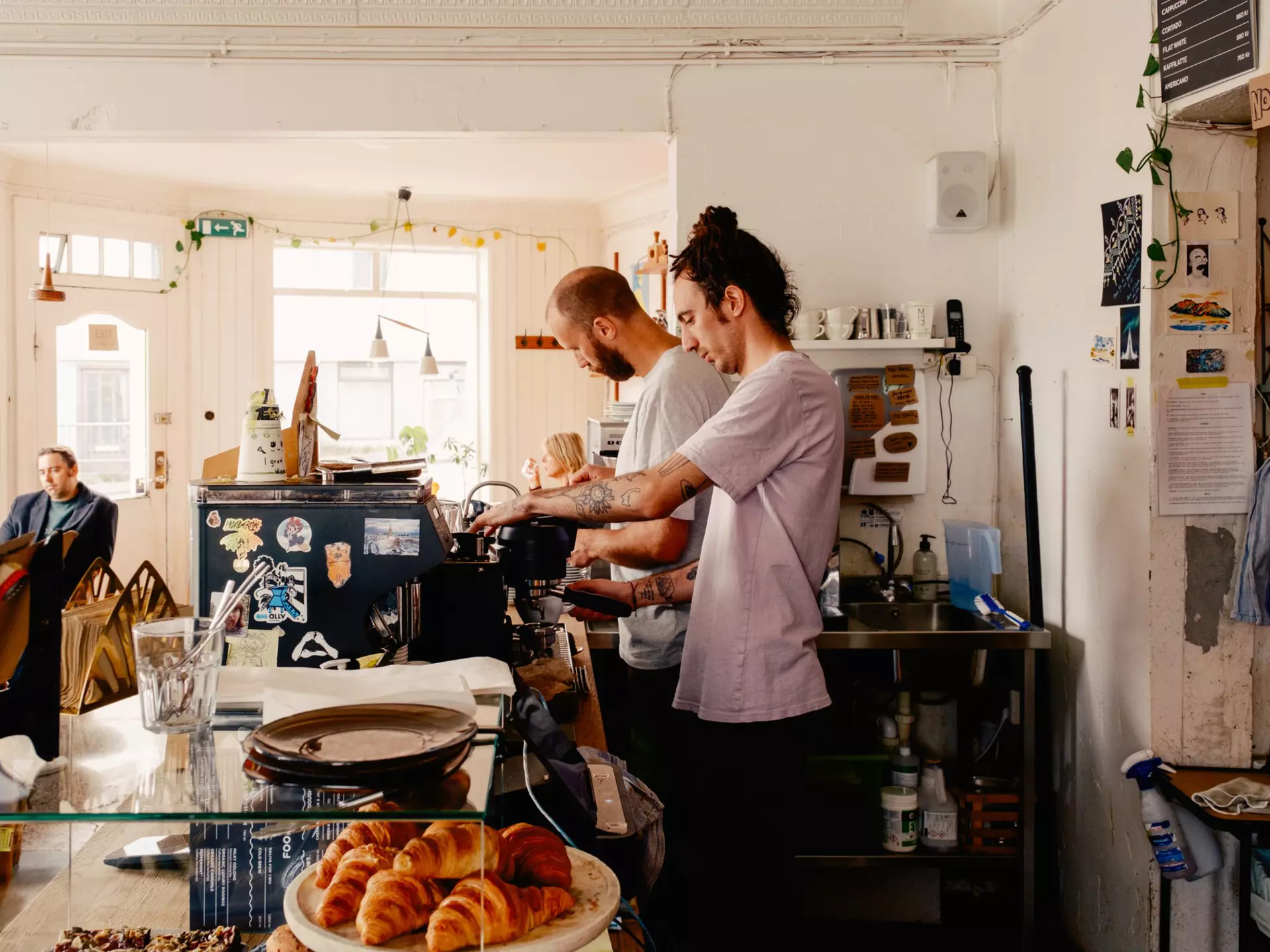 Two men prepare coffee drinks behind the counter of a cafe.