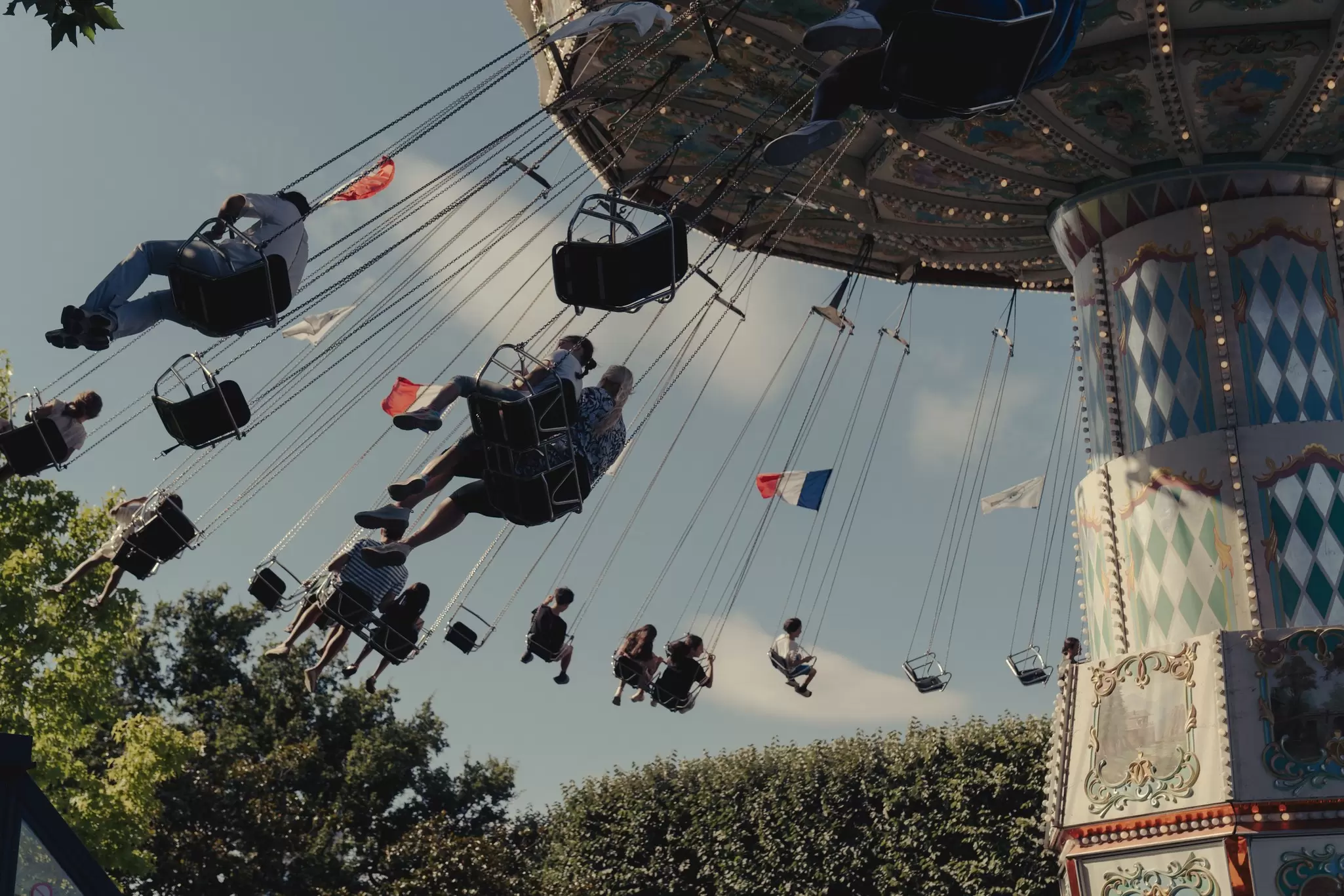 A vintage merry go round lifts riders up into the sky, with French flags attached to its chains