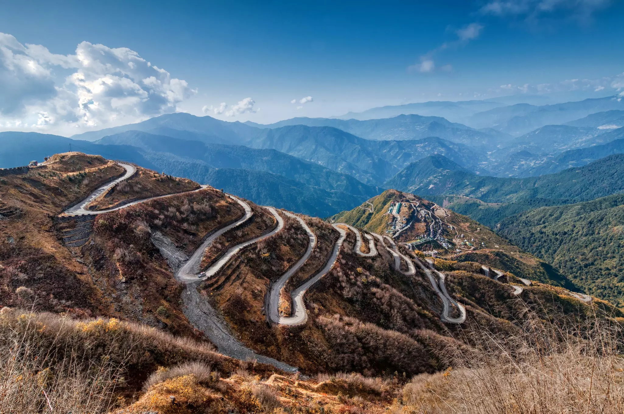 A single road winds its way up a steep mountain in Sikkim. With more mountains visible in the distance.