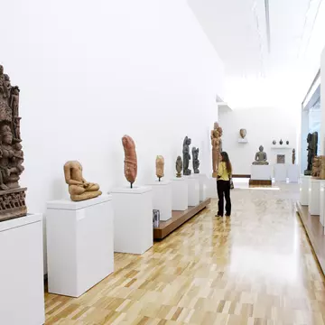 View of a long hallway with sculptures on either side. A woman is looking at a sculpture on one side of the hallway.