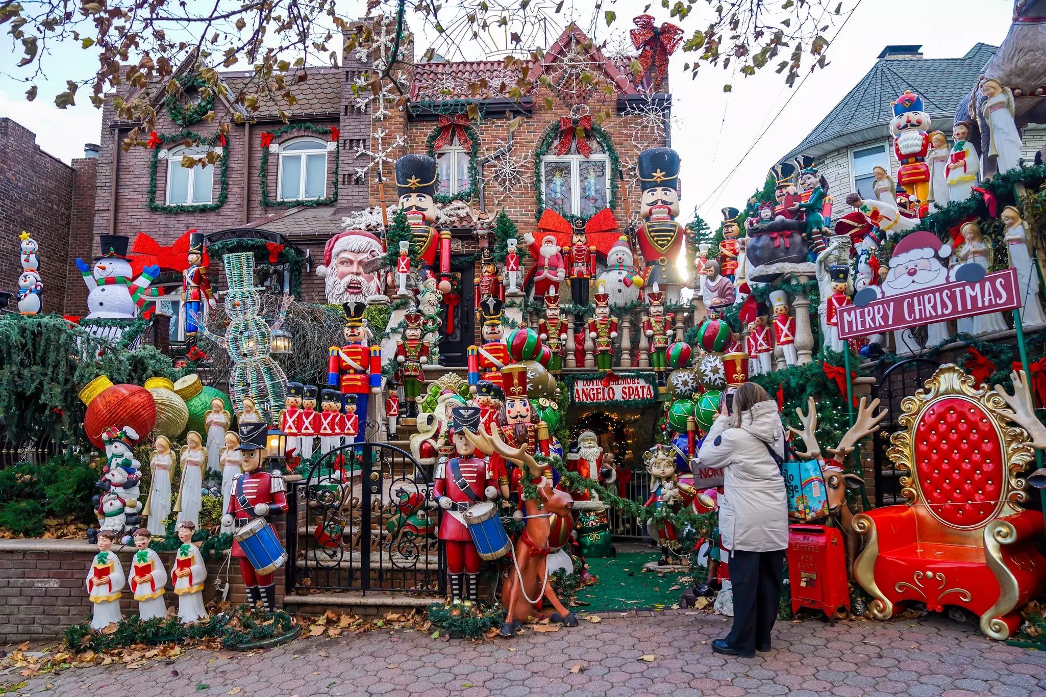 A brick home that is heavily decorated for Christmas. A woman is standing in front taking photos
