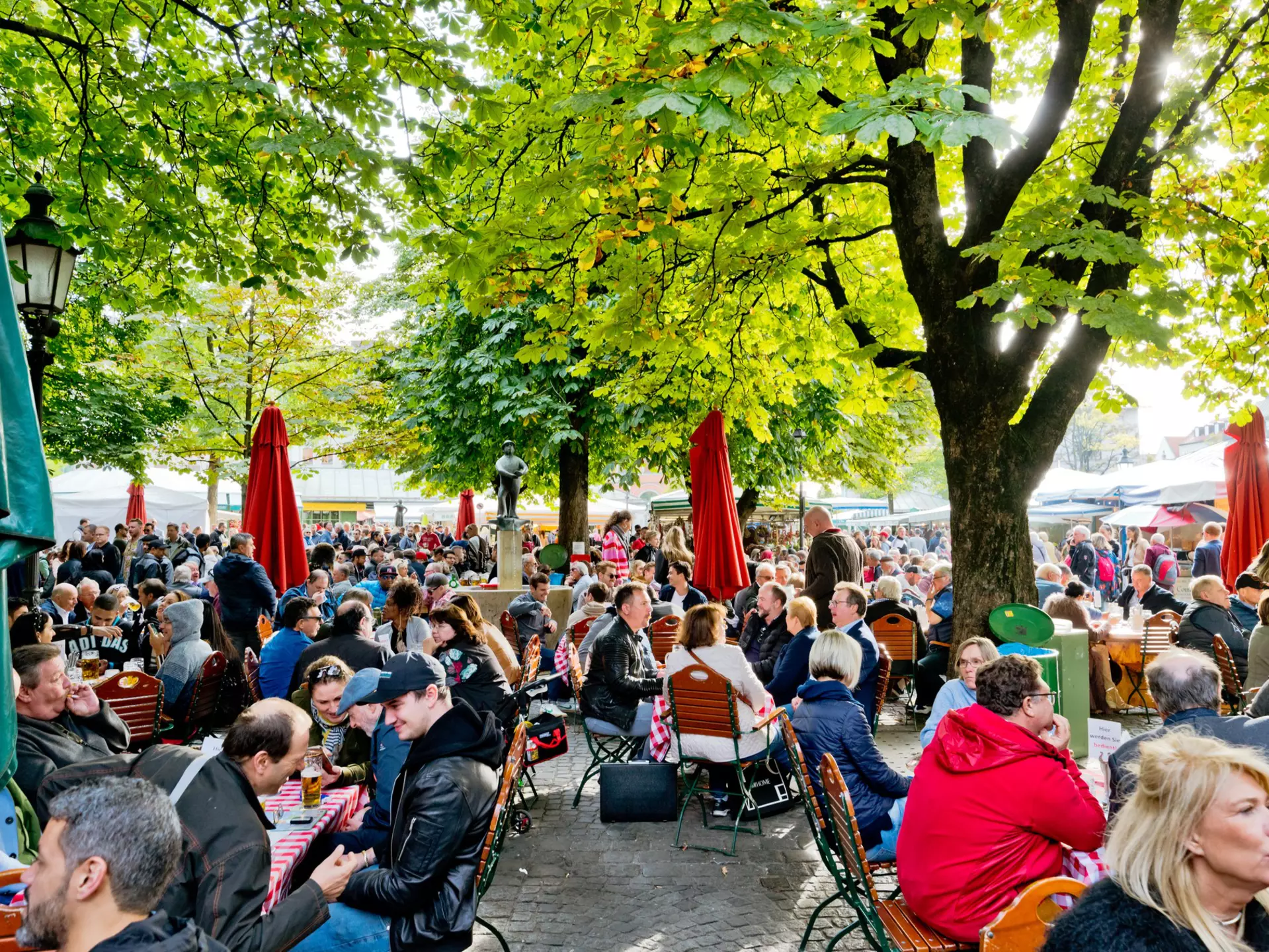 People sitting at the wooden tables enjoying the sunny weather drinking beer and eating traditional Bavarian food in Munich,