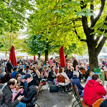 People sitting at the wooden tables enjoying the sunny weather drinking beer and eating traditional Bavarian food in Munich,