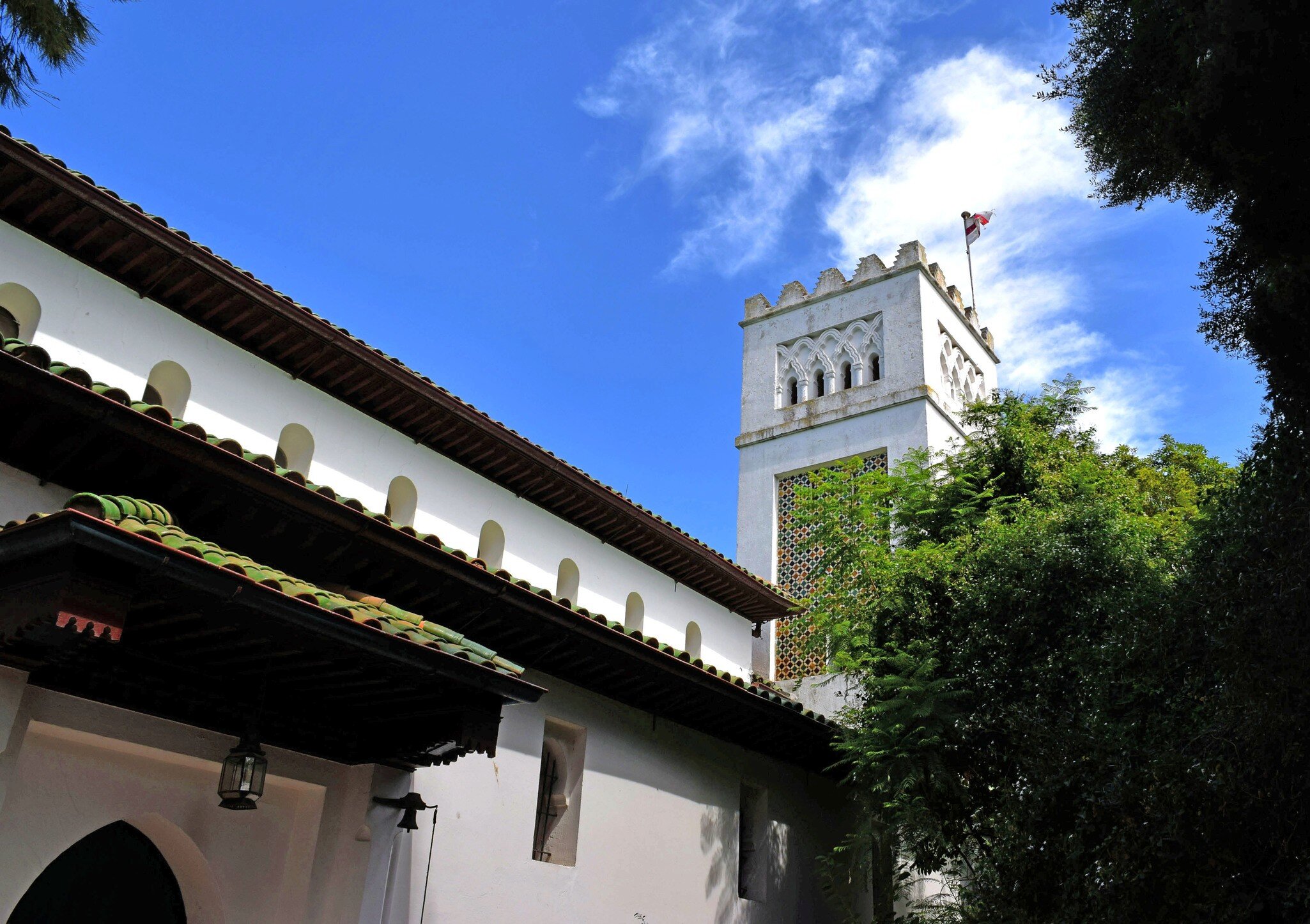 Whitewashed Moorish-style bell tower of St Andrew's Church above a tiled roof and trees in Tangier.