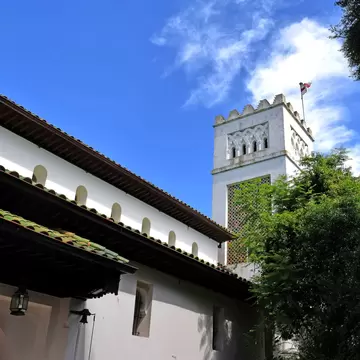 Whitewashed Moorish-style bell tower of St Andrew's Church above a tiled roof and trees in Tangier.