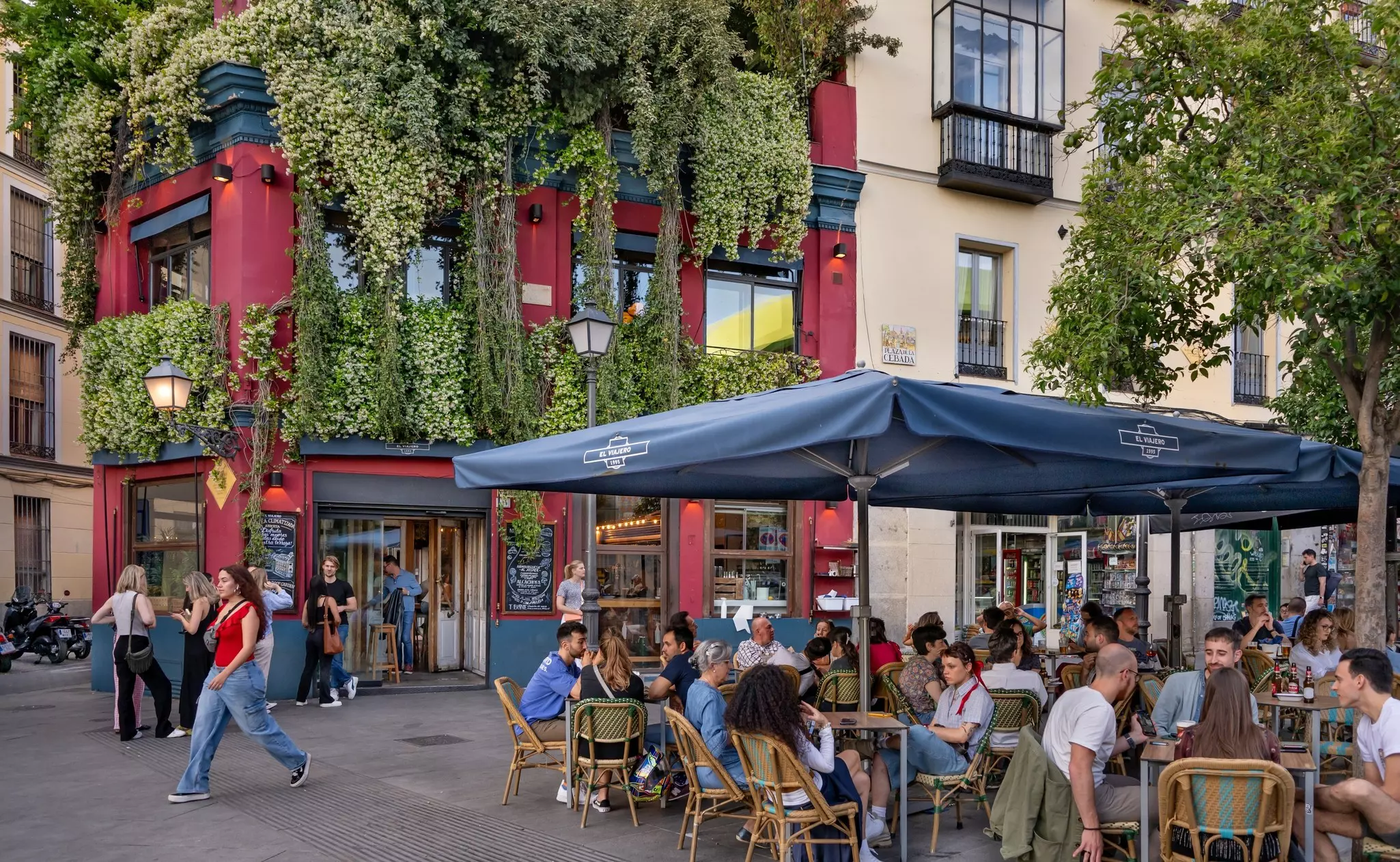 People sit at outdoor tables in a square in a city neighborhood.