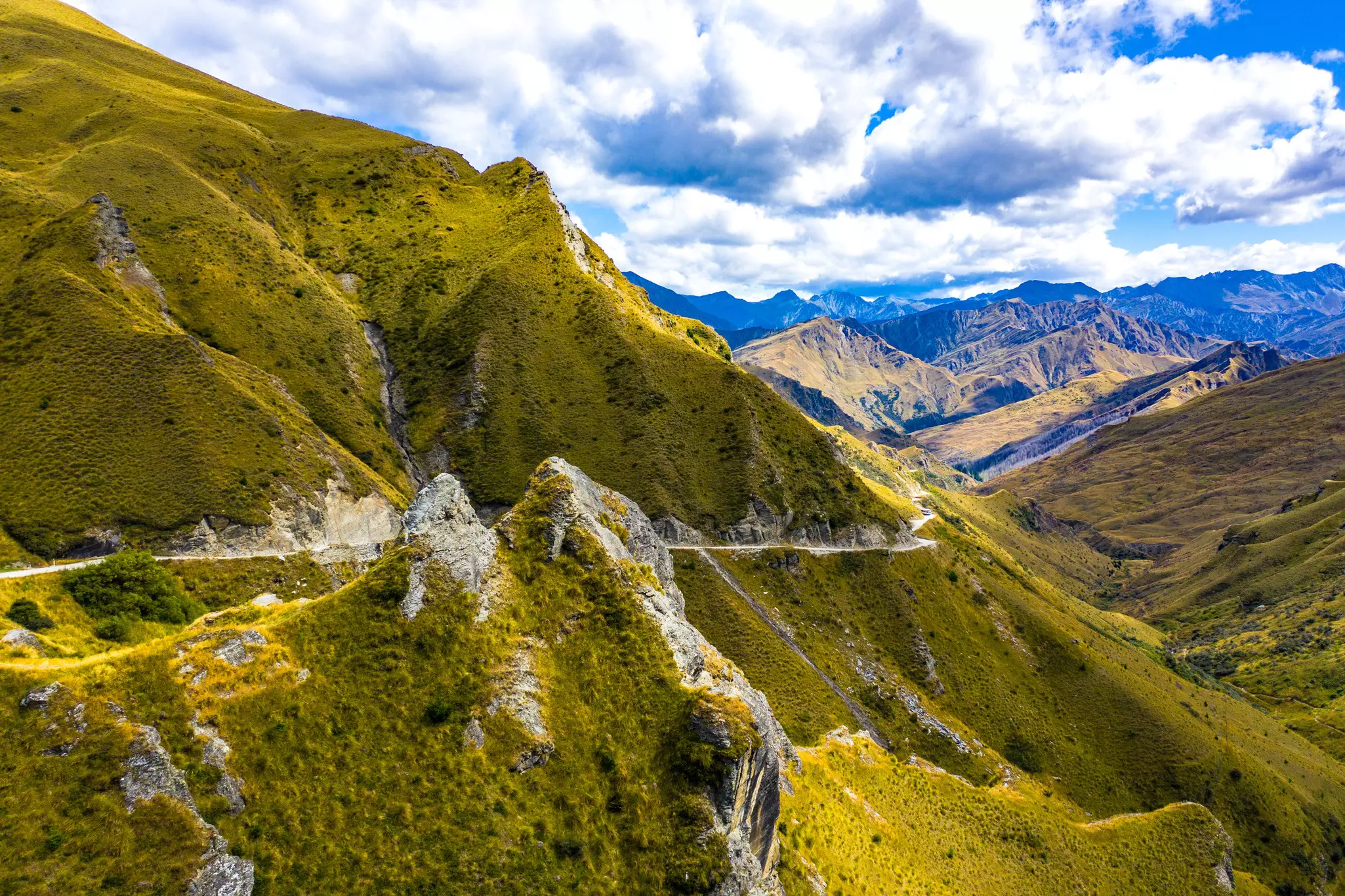 A rugged landscape with mountain peaks and a rough road at the edge of a hillside