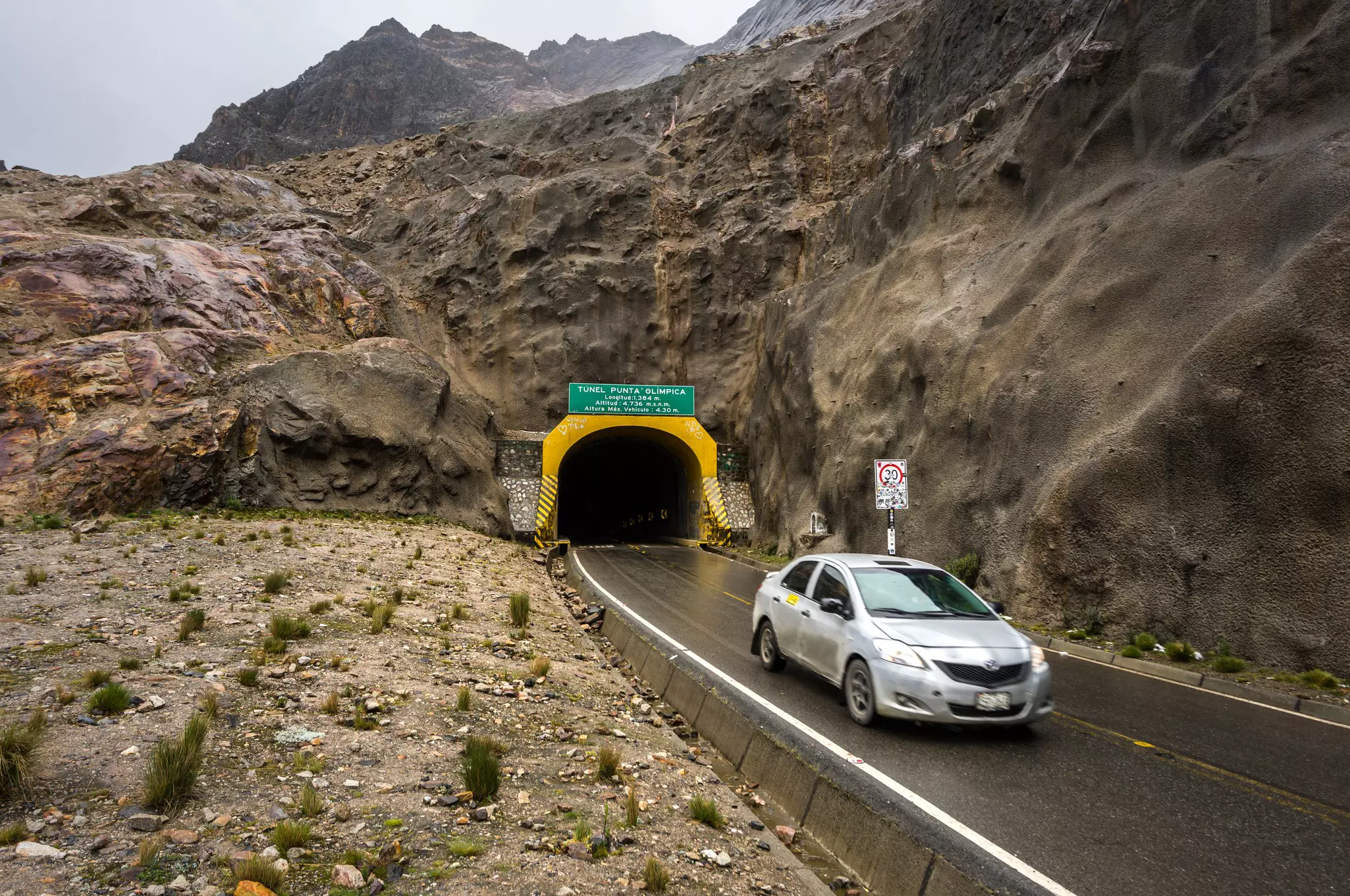 A car is pictured leaving a tunnel on a rainy day along a mountain road.
