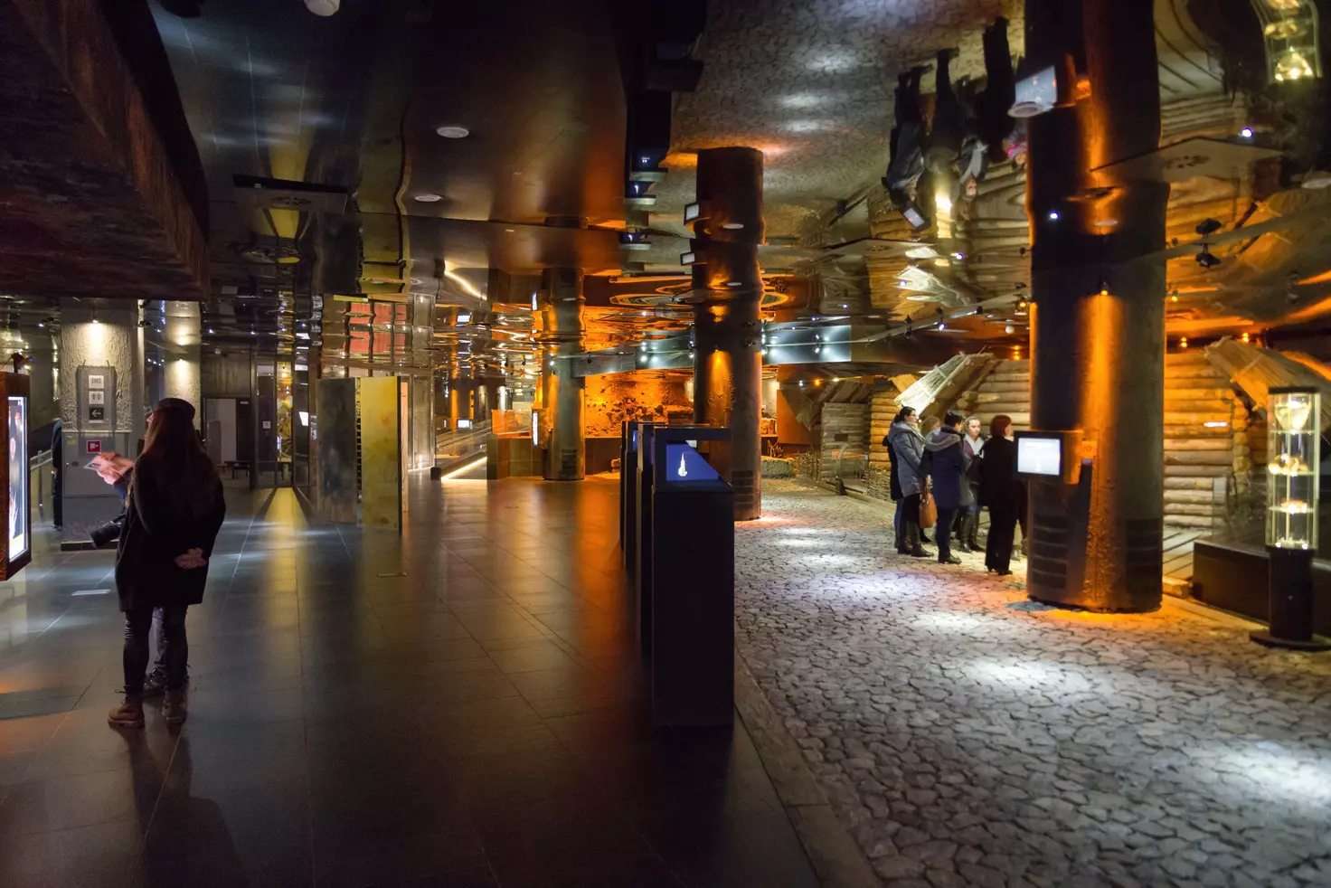 People looking at exhibits in the darkened gallery of an underground archaeology museum in Kraków.