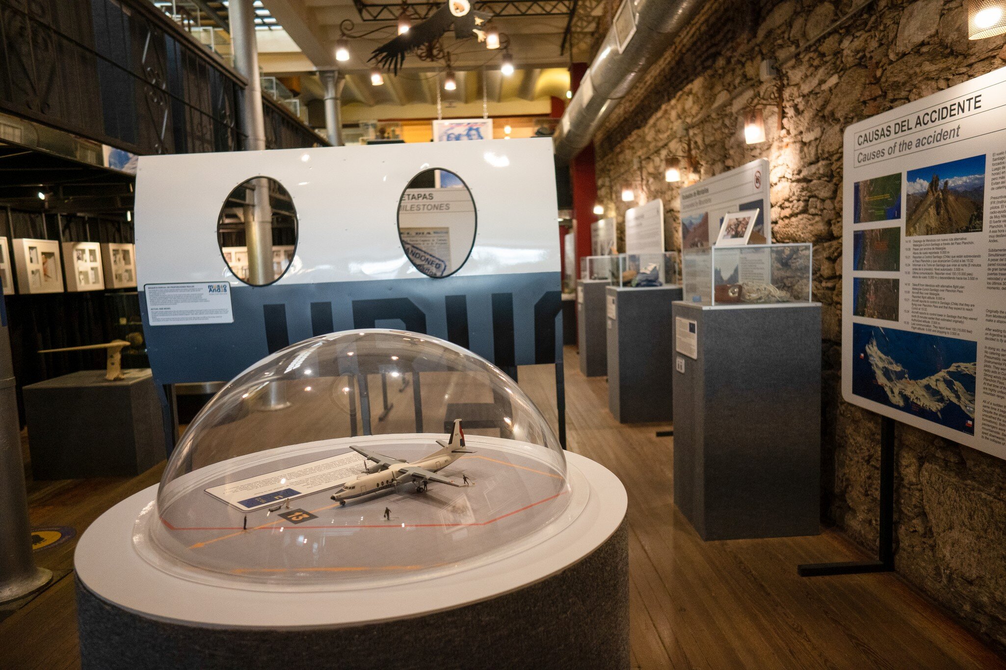 Model aircraft under a clear dome in a stone-walled museum gallery lined with display cases and panels.