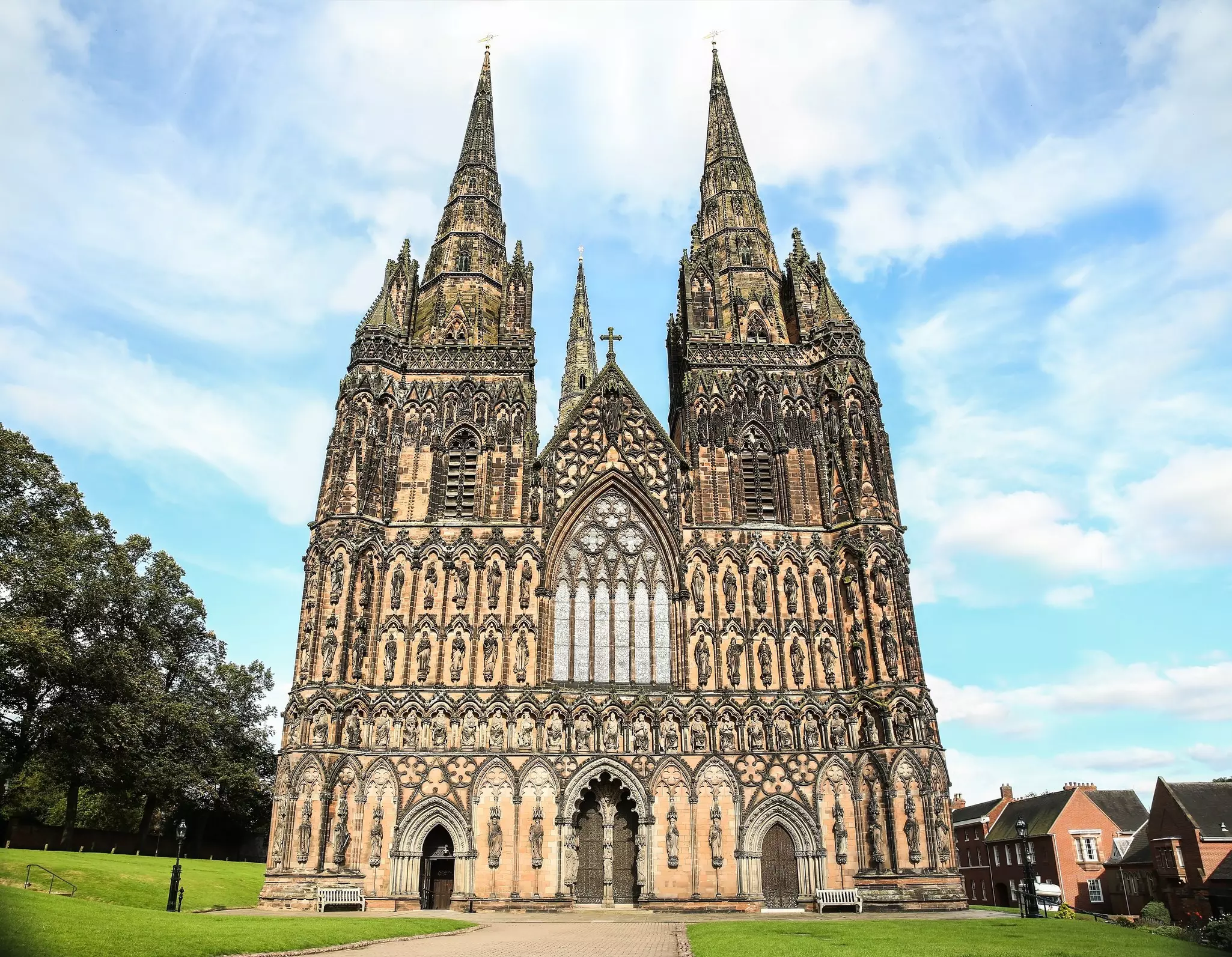Looking up at the elaborate Gothic facade of a three-spired stone cathedral covered in statuary.