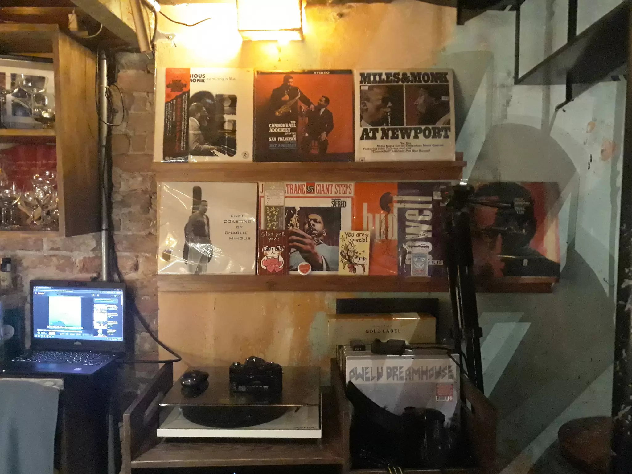 Classic albums on shelves along a wall above a record player. A laptop is open on a table at the left.