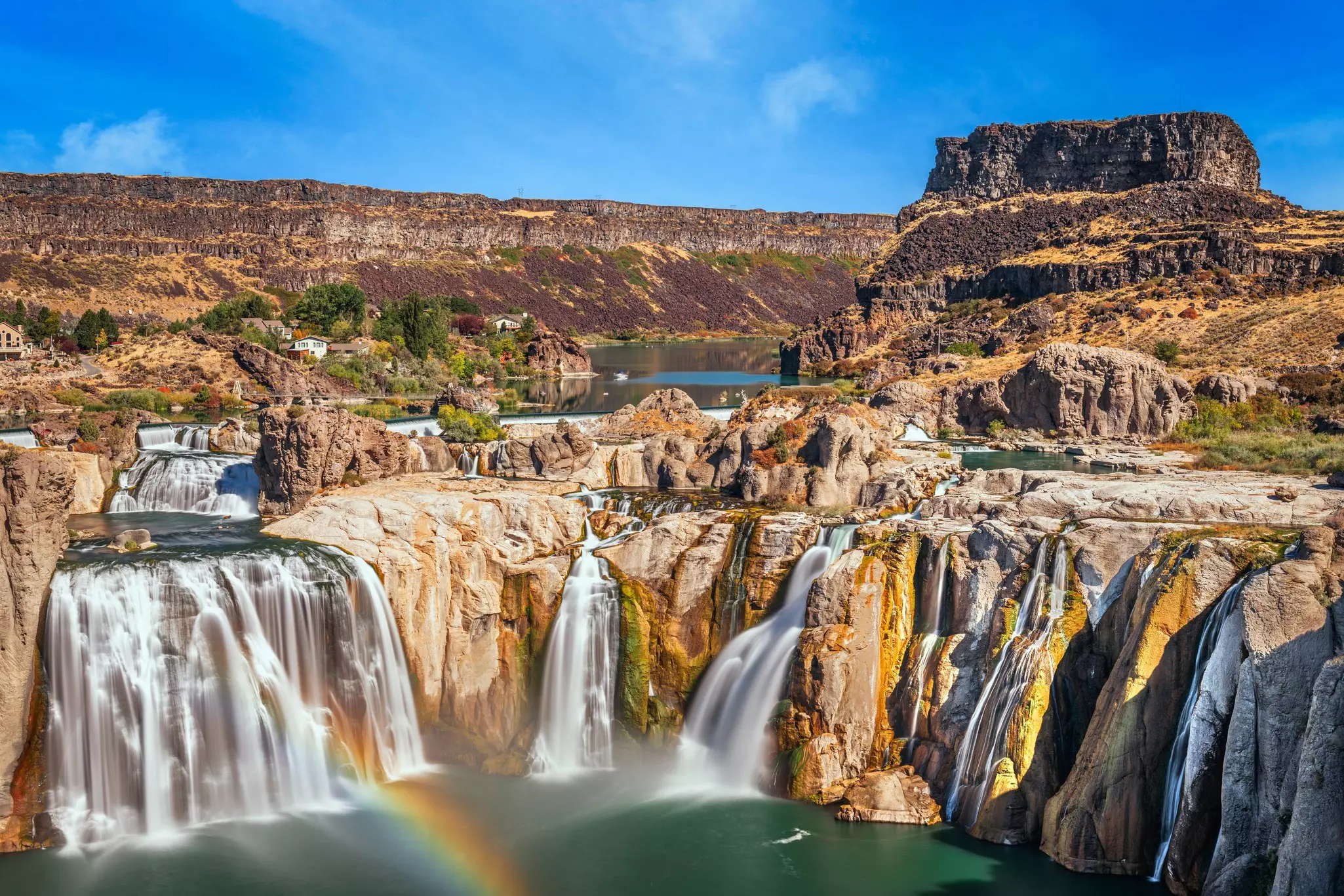 A series of waterfalls cascade down sending up spray that creates a rainbow