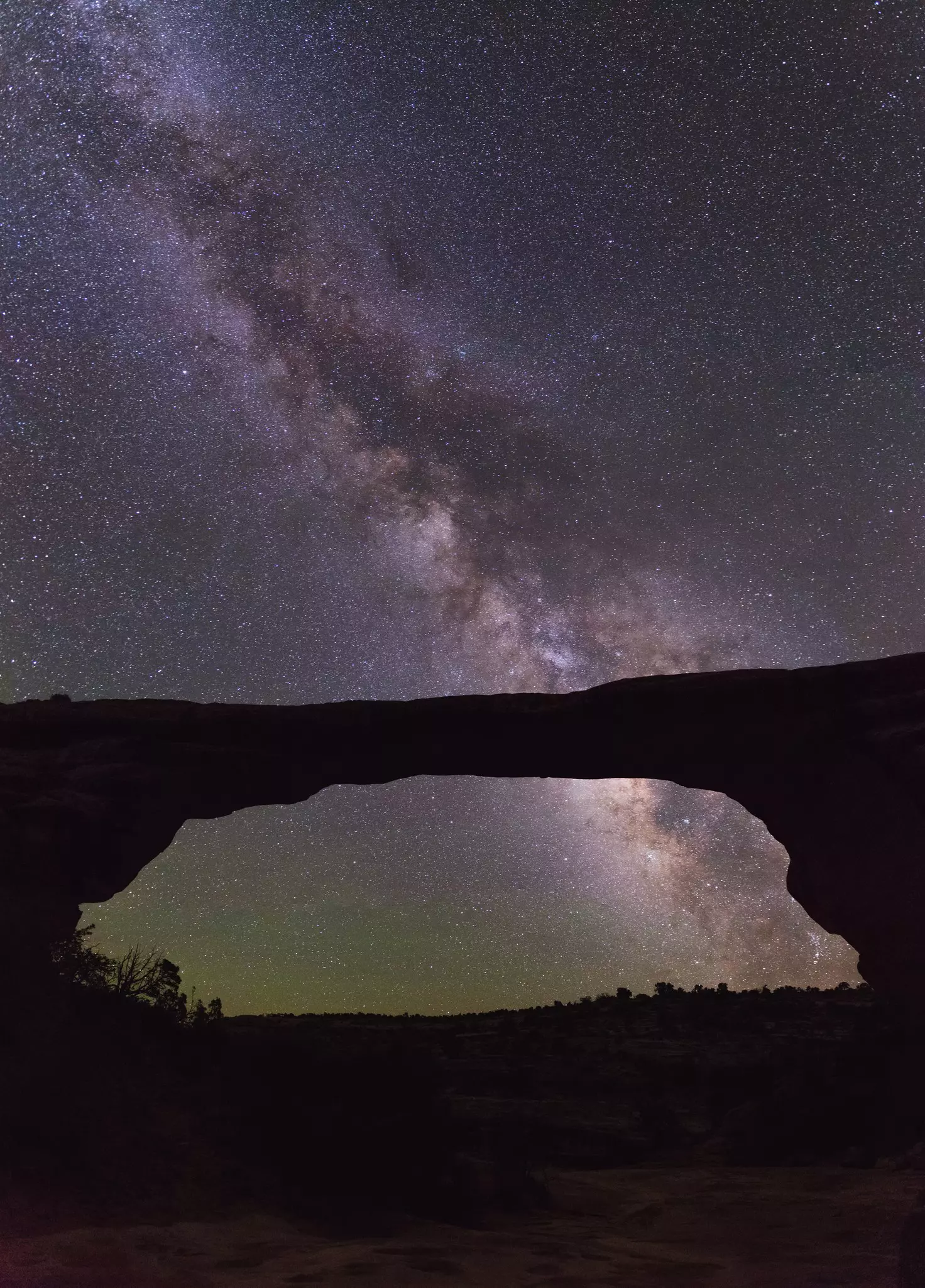 A large natural rock arch silhouetted against a  starry night sky