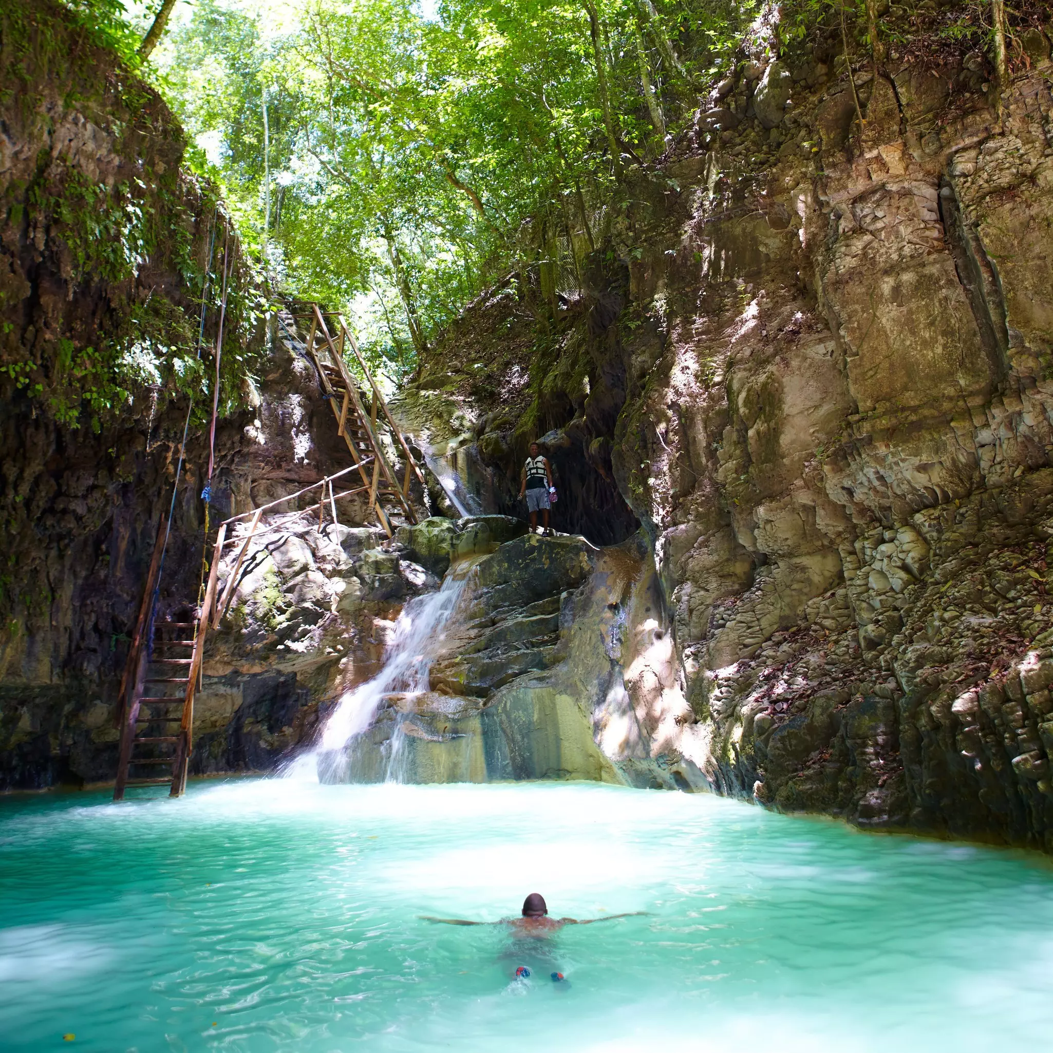 A man swimming in a lagoon with rocks and a ladder