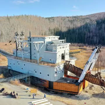 Huge timber gold dredge with a rusted bucket line resting in a valley of autumn birch and spruce near Dawson City