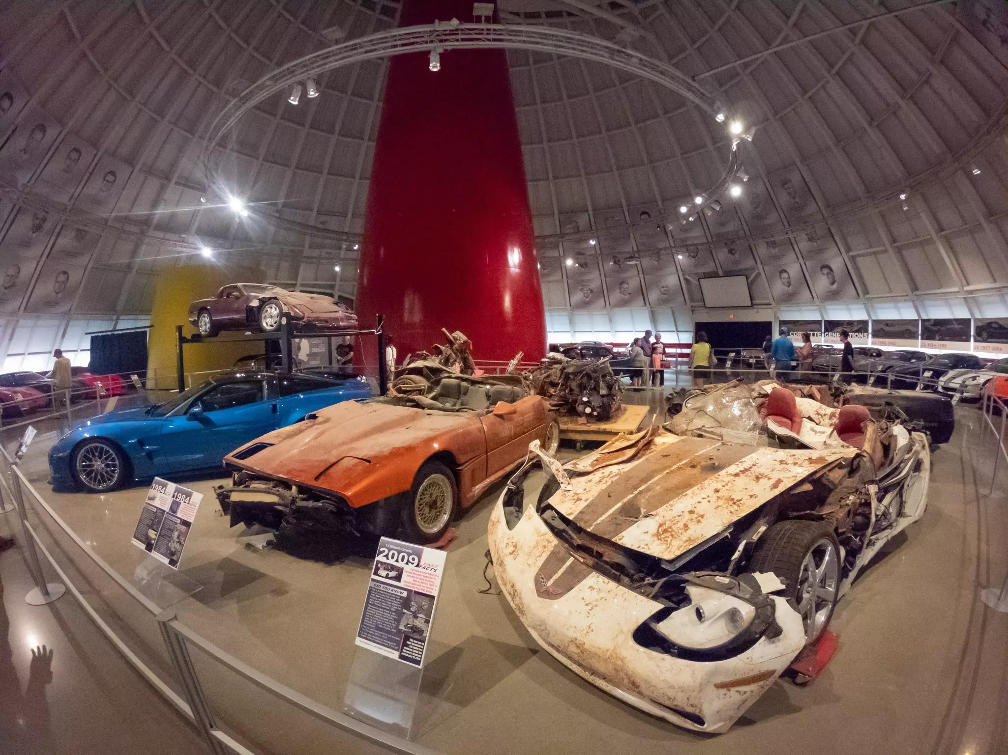Various sports cars in different states of repair are on display in a large gallery with a domed roof.