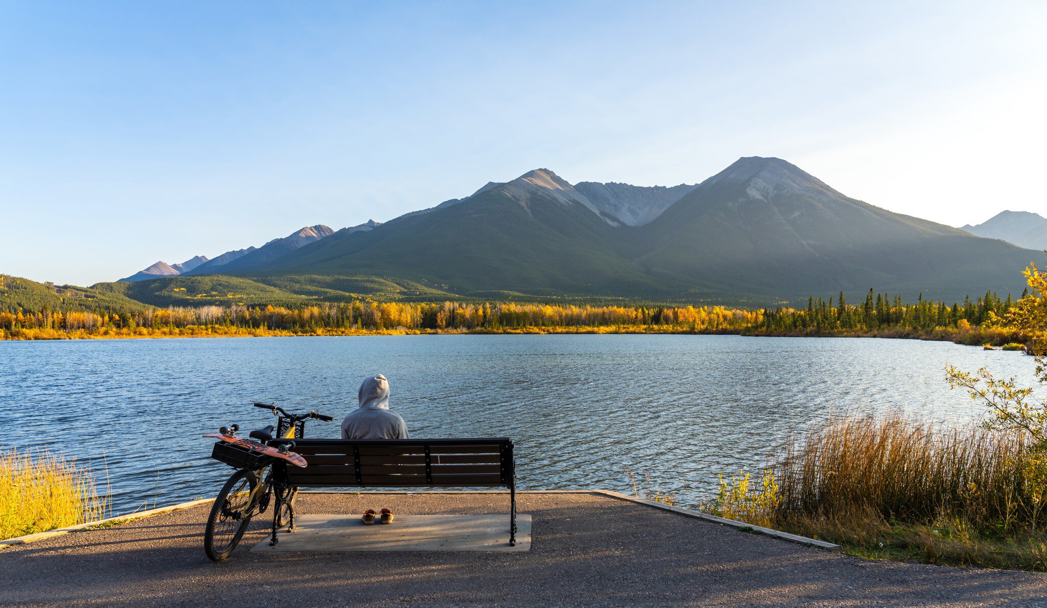 Tourist resting on wooden bench, relaxing at Vermilion Lakes lakeshore in autumn foliage season sunset time. Cycling in Banff National Park Legacy Trail. Canadian Rockies, Alberta, Canada., License Type: media, Download Time: 2025-11-27T22:11:52.000Z, User: claramonitto, Editorial: false, purchase_order: 56530 - Guidebooks, job: Global Publishing-WIP, client: Best Bike Rides Canada 1 , other: Clara Monitto