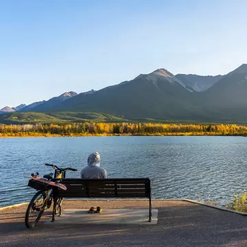 Tourist resting on wooden bench, relaxing at Vermilion Lakes lakeshore in autumn foliage season sunset time. Cycling in Banff National Park Legacy Trail. Canadian Rockies, Alberta, Canada., License Type: media, Download Time: 2025-11-27T22:11:52.000Z, User: claramonitto, Editorial: false, purchase_order: 56530 - Guidebooks, job: Global Publishing-WIP, client: Best Bike Rides Canada 1 , other: Clara Monitto
