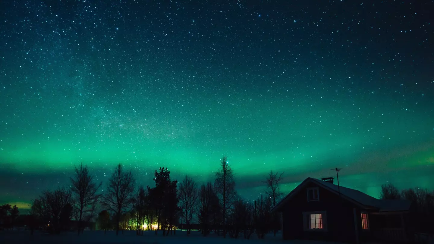 The Northern Lights (Aurora Borealis) over snowed-in cottage in Lapland village. Finland