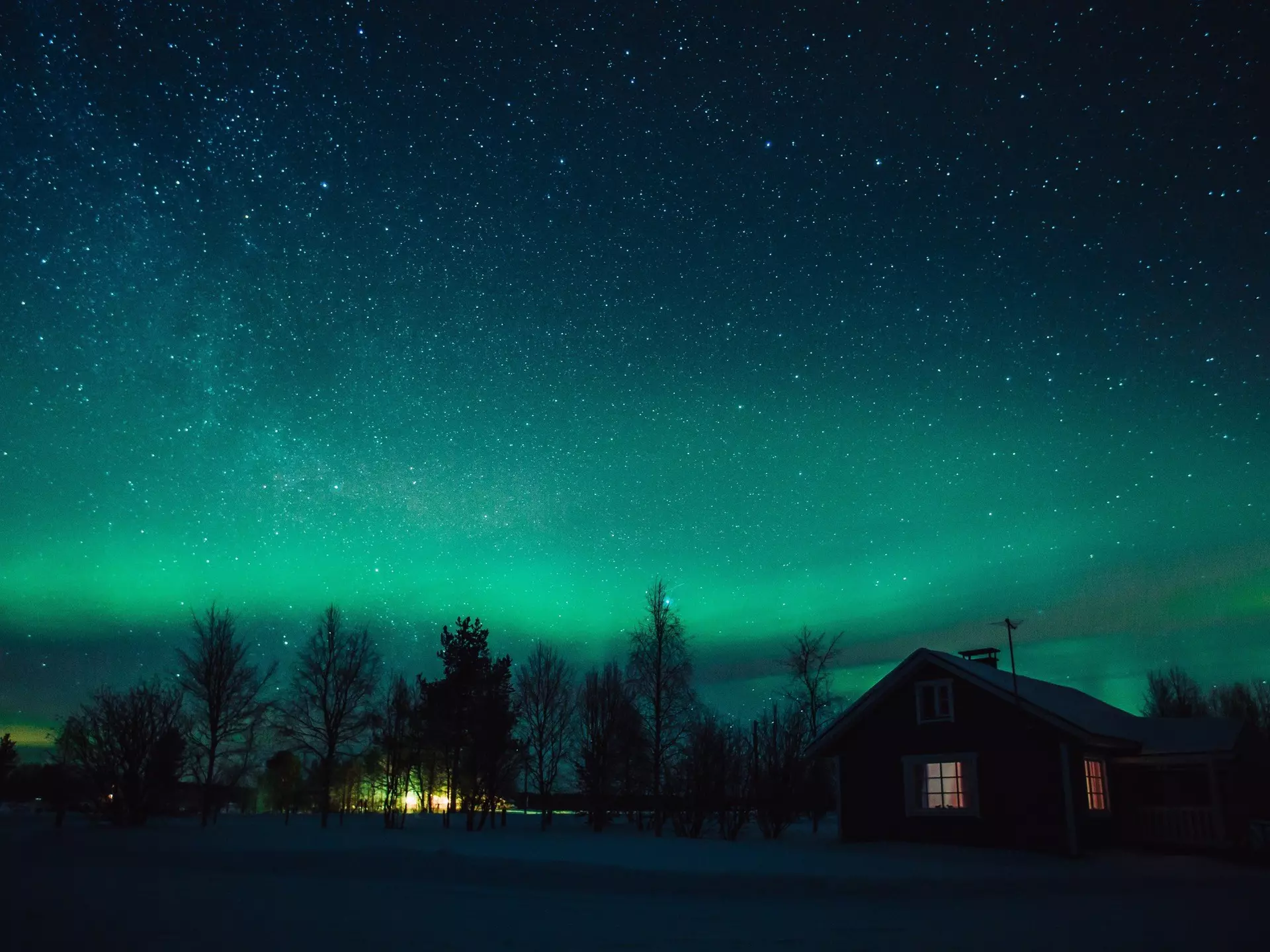 The Northern Lights (Aurora Borealis) over snowed-in cottage in Lapland village. Finland