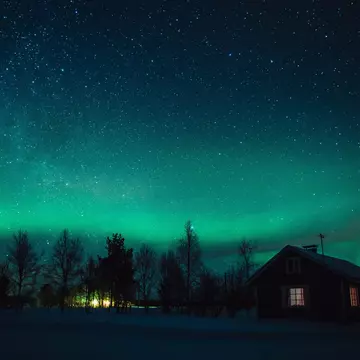 The Northern Lights (Aurora Borealis) over snowed-in cottage in Lapland village. Finland