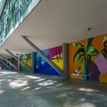A long open-sided concrete canopy on slender columns, a bright mural along the wall beneath it.