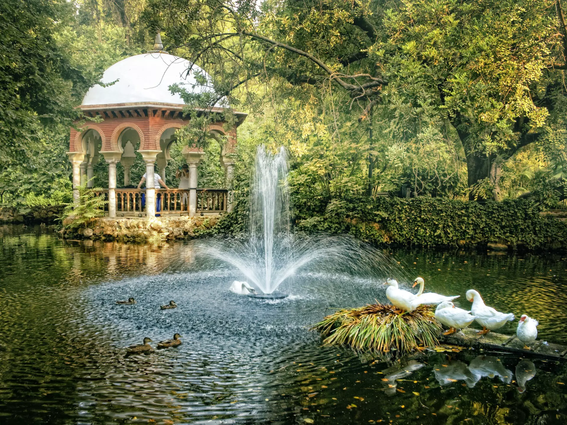 A Moorish-style pavilion by a pond with white ducks at María Luisa Park, Seville, Spain