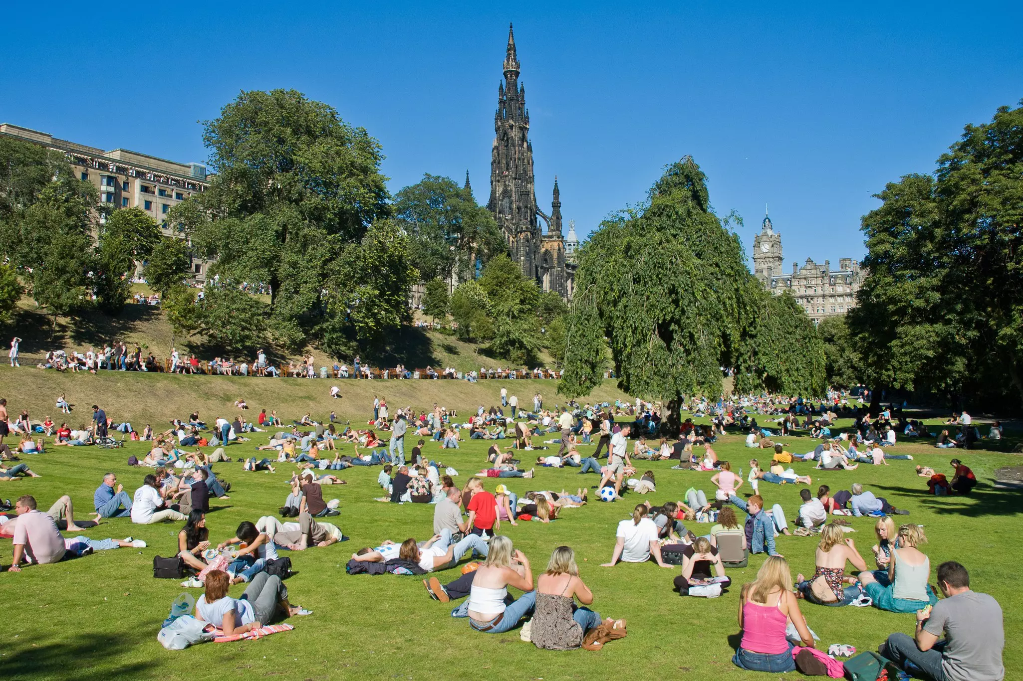 People enjoying the sun in Princes Street Garden, Edinburgh, with the Scott Monument rising behind.