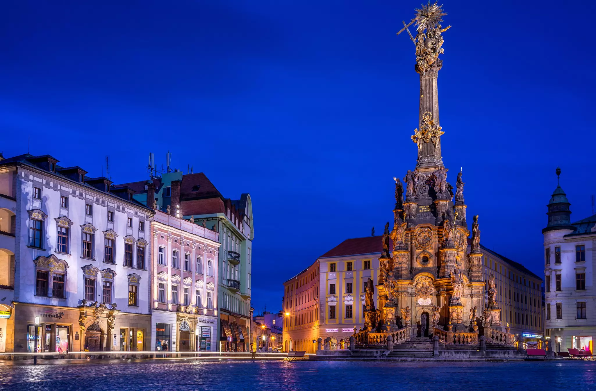 A large baroque sculpture adorned with religious symbols and figures in the center of a city square at night