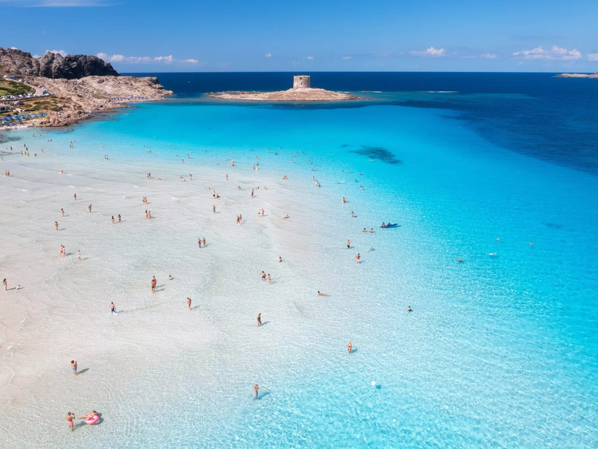 Aerial view of famous La Pelosa beach at sunny summer day. Stintino, Sardinia island, Italy. Top view of sandy beach, swimming people, clear blue sea, old tower and sky with clouds. 