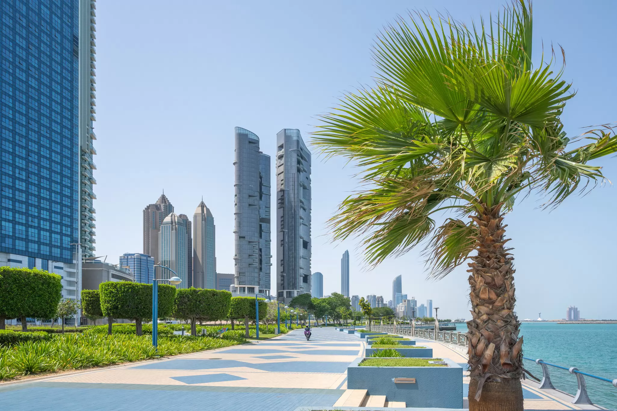 A palm tree and skyscrapers frame the view along the Corniche in Abu Dhabi, UAE.