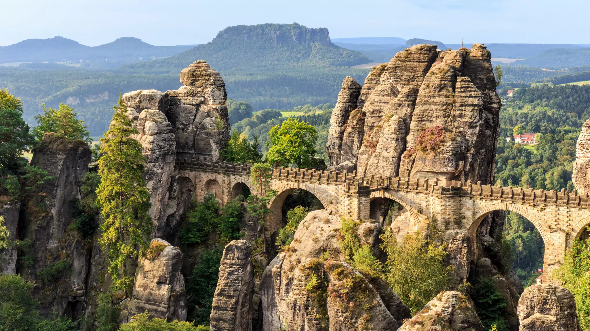 A stone bridge with arches connects rock formations in a country landscape.