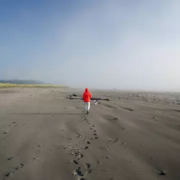 A white-coated beachgoer walks along at brown sands of Seaview, on Long Beach peninsula, Washington