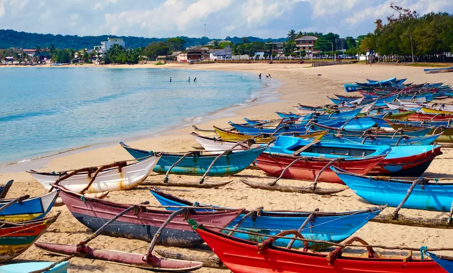 Trincomalee, Sri Lanka: rows of colourful outrigger fishing canoes on a curving sandy bay, swimmers in calm water
