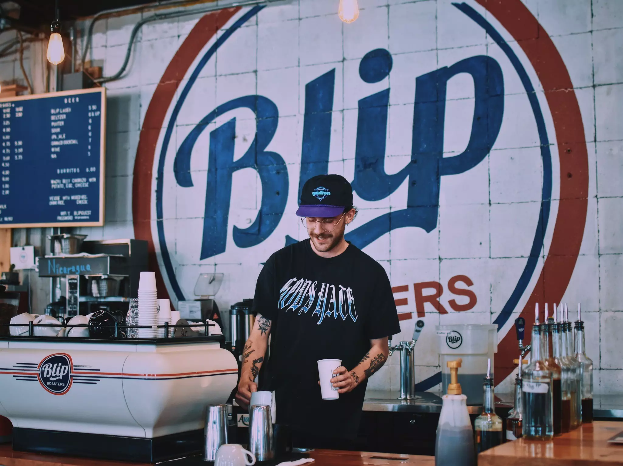A barista makes a coffee in front of a mural at a loft-like coffee shop.
