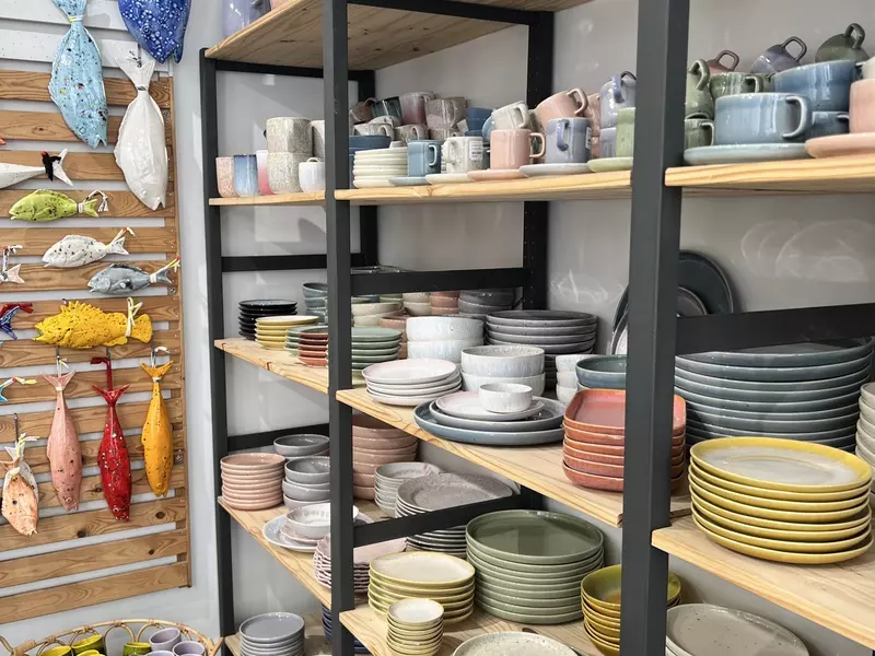 Colorful pottery plates and bowls are stacked on shelves, and ceramic fish are displayed on the wall.